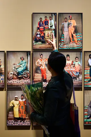 A person holding a bouquet of flowers taking a photo of an display of framed photographs with a mobile phone.